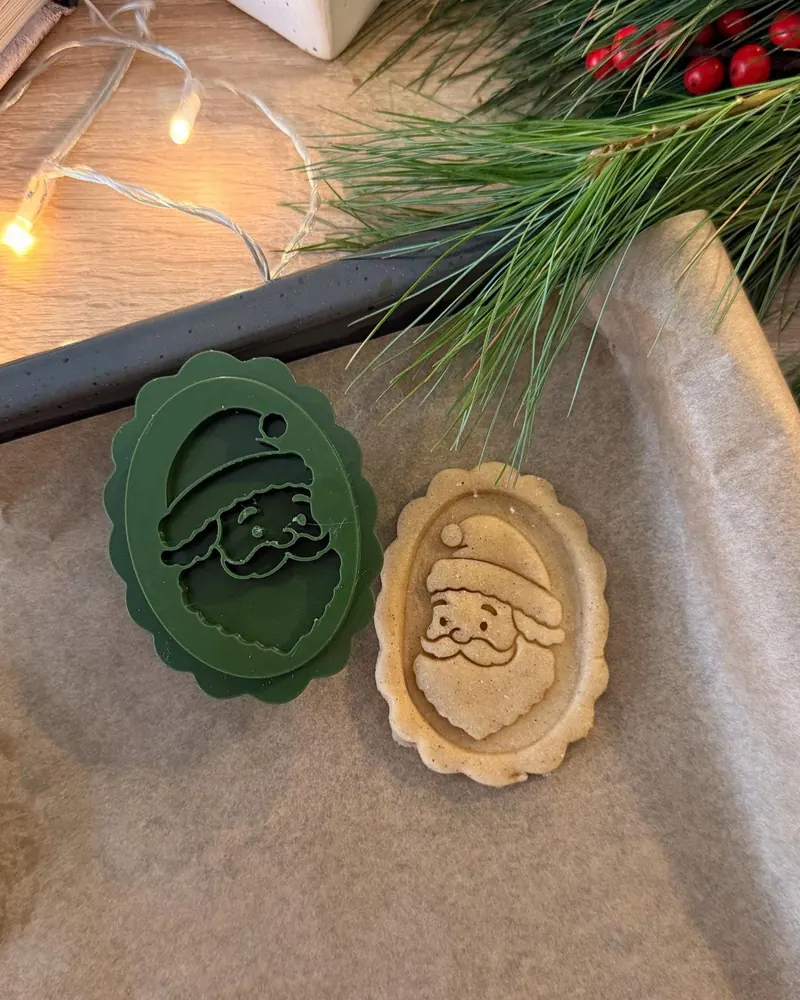 Green Santa cookie stamp next to a stamped Santa cookie, with pine and fairy lights