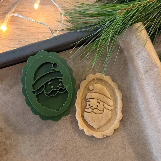 Green Santa cookie stamp next to a stamped Santa cookie, with pine and fairy lights