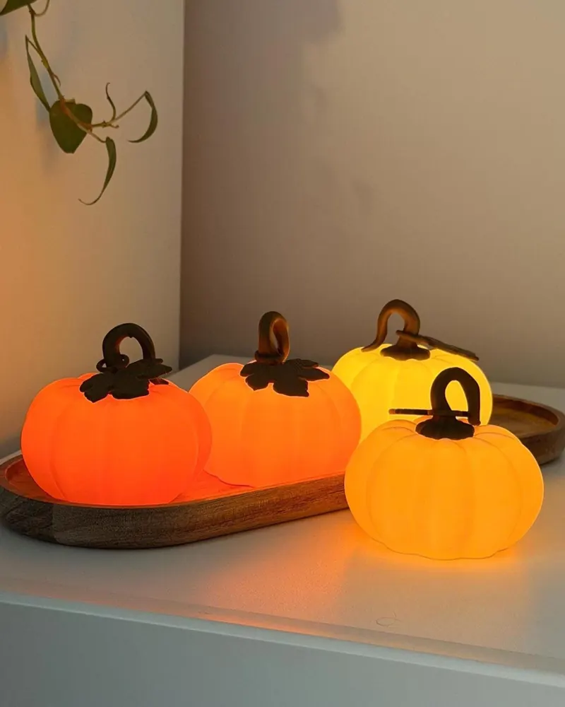 Four glowing pumpkin night lights in orange and yellow on a wooden tray